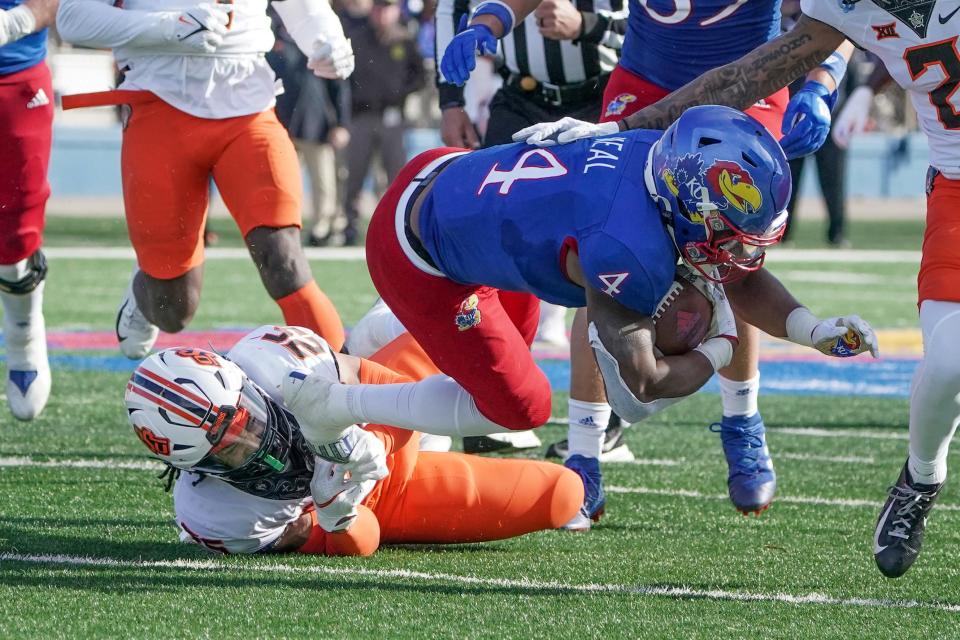 Kansas Jayhawks running back Devin Neal (4) runs the ball as Oklahoma State Cowboys safety Jason Taylor II (25) makes the tackle during the first half of the game at David Booth Kansas Memorial Stadium.