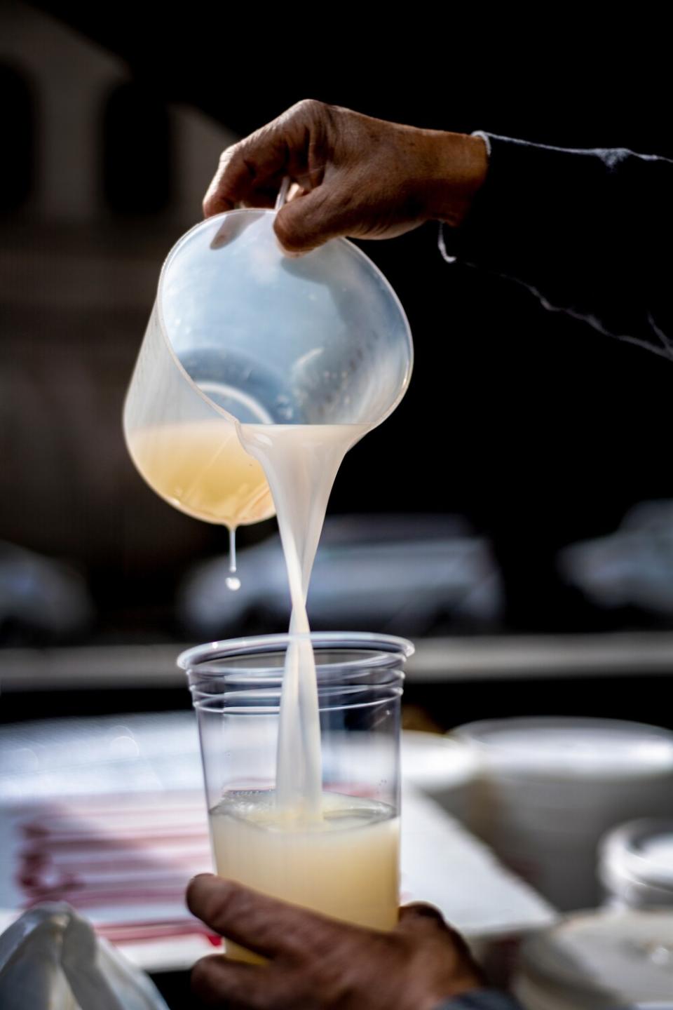 A man pours pulque from one container into another.