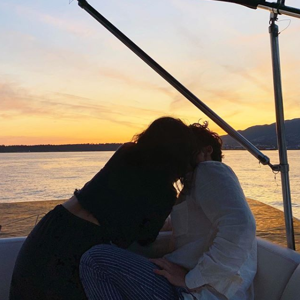 A photo of Riverdale couple Camila Mendes and Charles Melton sharing a kiss on a boat at sunset.