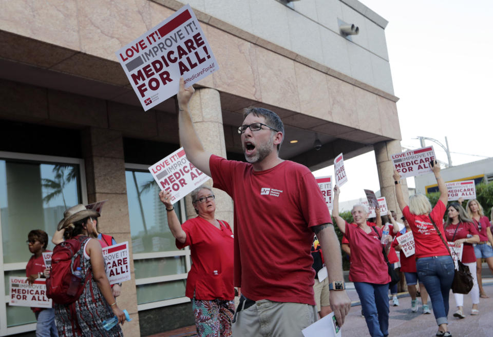 People with National Nurses United march in support of medicare for all, outside of the Knight Concert Hall at the Adrienne Arsht Center for the Performing Arts of Miami-Dade County, where a Democratic presidential debate is taking place, Wednesday, June 26, 2019, in Miami. (AP Photo/Lynne Sladky)