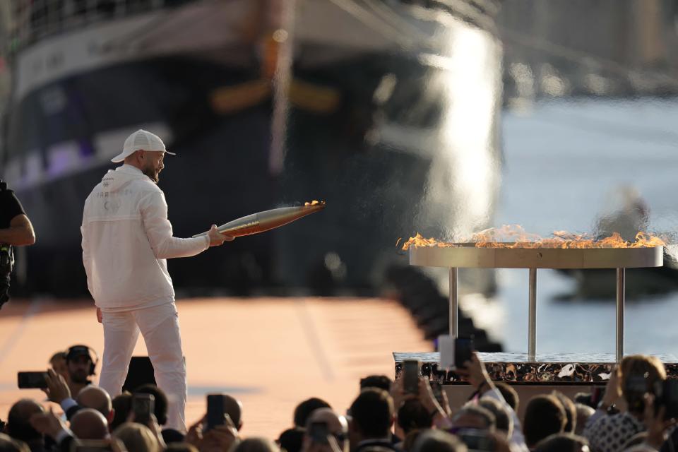 French rap artist Jul lights the Olympic cauldron with the Olympic torch during the torch arrival ceremony in Marseille, southern France, Wednesday May 8, 2024. After leaving Marseille, a vast relay route is undertaken before the torch odyssey ends on July 27 in Paris. The Paris 2024 Olympic Games will run from July 26 to Aug.11, 2024. (AP Photo/Thibault Camus)