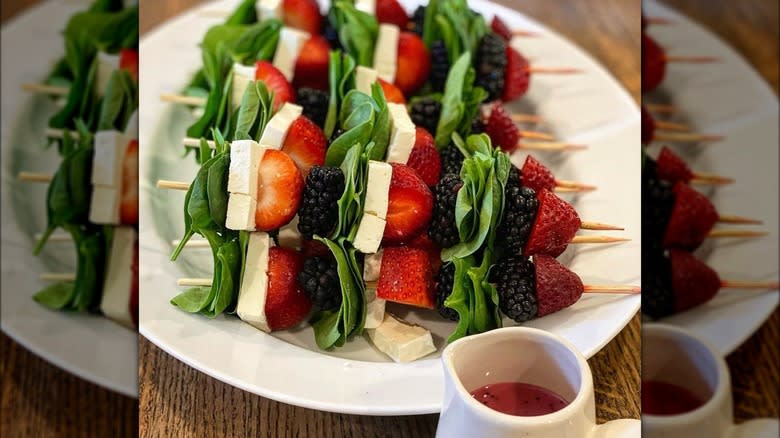 salad skewers on plate with spinach, berries, and cheese