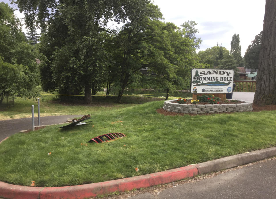 In this photo taken Tuesday, June 25, 2019, provided by the Washougal Police Department, police tape and debris are seen at the Sandy Swimming Hole Park in Washougal, Wash. A man accused of driving his Jeep through a fence at the Washington state swimming hole and running over two German tourists, killing them, has been arrested. (Washougal Police Department via AP)