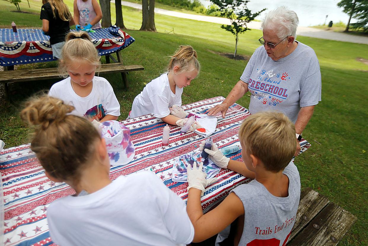 Donna Messerly (right) gives Raegan Garver some pointers as she works to tie-dye her hat along with her brother Lincoln and sisters Kennedy and Kinley during a messy camp activity at Charles Mill Lake last week.