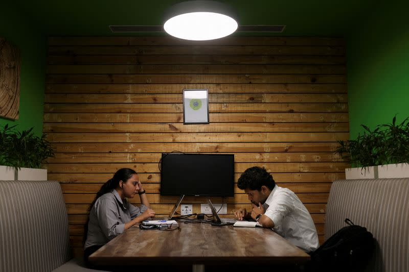 FILE PHOTO: People sit and work on their laptops at Deloitte's office in Gurugram