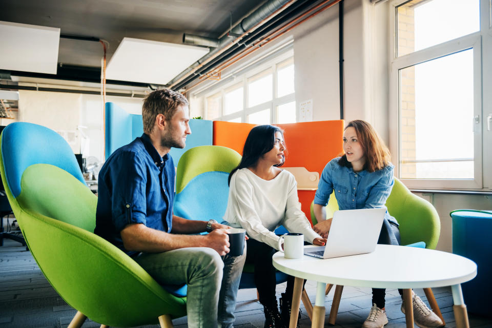 Three colleagues sitting in colorful chairs and talking with each other during a meeting in a bright and modern office environment.