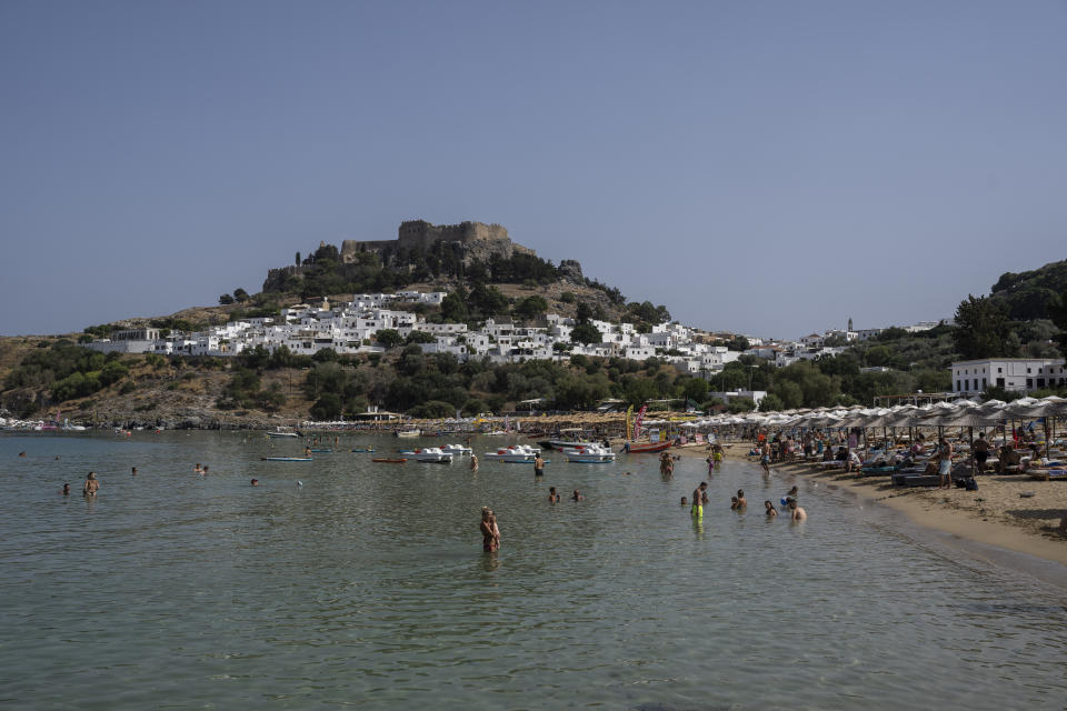 FILE - Tourists enjoy the beach and the sea in Lindos, on the Aegean Sea island of Rhodes, southeastern Greece, on July 27, 2023. Tourists at a seaside hotel on the Greek island of Rhodes snatched up pails of pool water and damp towels as flames approached, rushing to help staffers and locals extinguish one of the wildfires threatening Mediterranean locales during recent heat waves. (AP Photo/Petros Giannakouris, File)