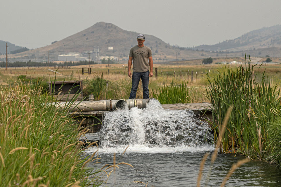 FILE - Justin Grant watches water flow from his agricultural well, Saturday, July 24, 2021, in Klamath Falls, Ore. Dozens of domestic wells have gone dry in an area near the Oregon-California border where the American West's worsening drought has taken a particularly dramatic toll. (AP Photo/Nathan Howard)