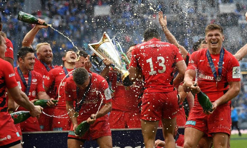 Saracens players celebrate with champagne and the Champions Cup trophy.