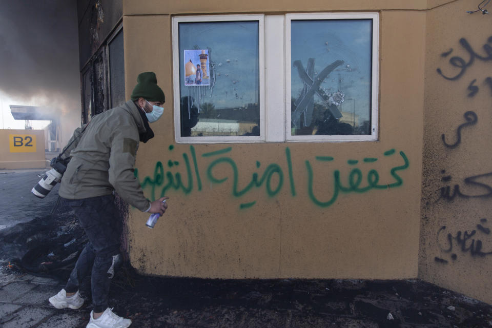 A man sprays a slogan that reads "the Martyrs wish is fulfilled," at the wall of the U.S. embassy, in Baghdad, Iraq, Wednesday, Jan. 1, 2020. Iran-backed militiamen have withdrawn from the U.S. Embassy compound in Baghdad after two days of clashes with American security forces. (AP Photo/Nasser Nasser)