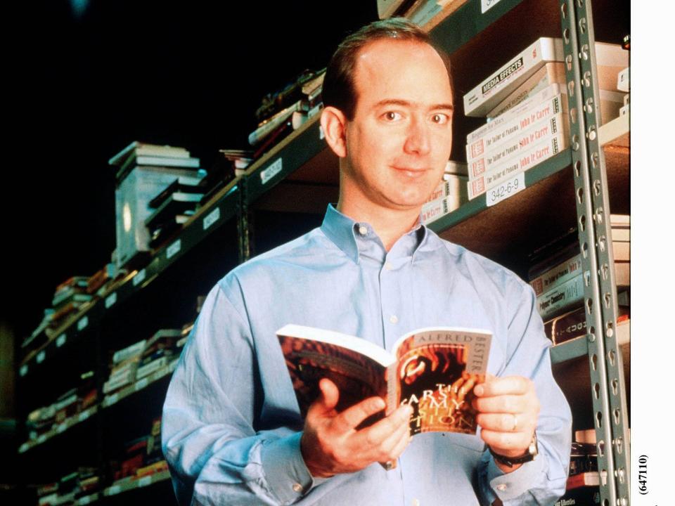 Jeff Bezos holds book and poses against book rack
