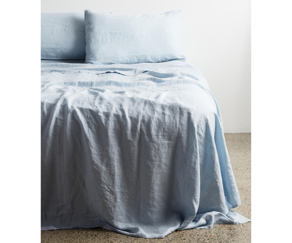 An image of a bed in pale blue bed linen with a white wall behind and a polished concrete floor.