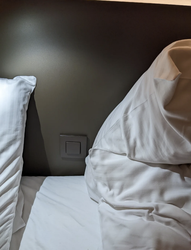 Bed with white sheets and pillows, next to a headboard with a square switch