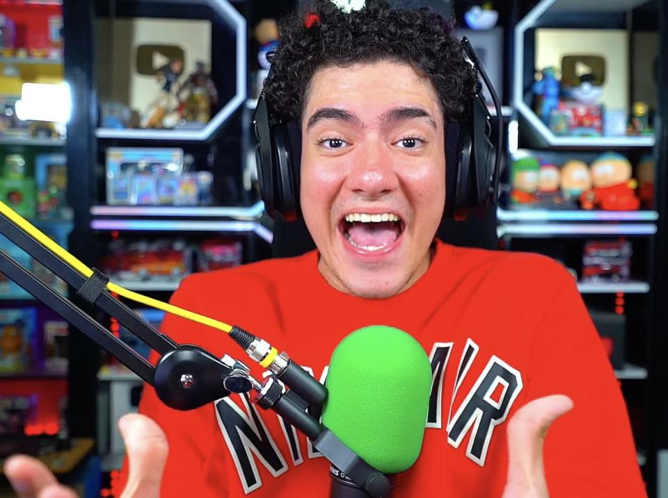 Screenshot from The Donato's YouTube channel, wearing a red sweater and speaking into a green microphone.