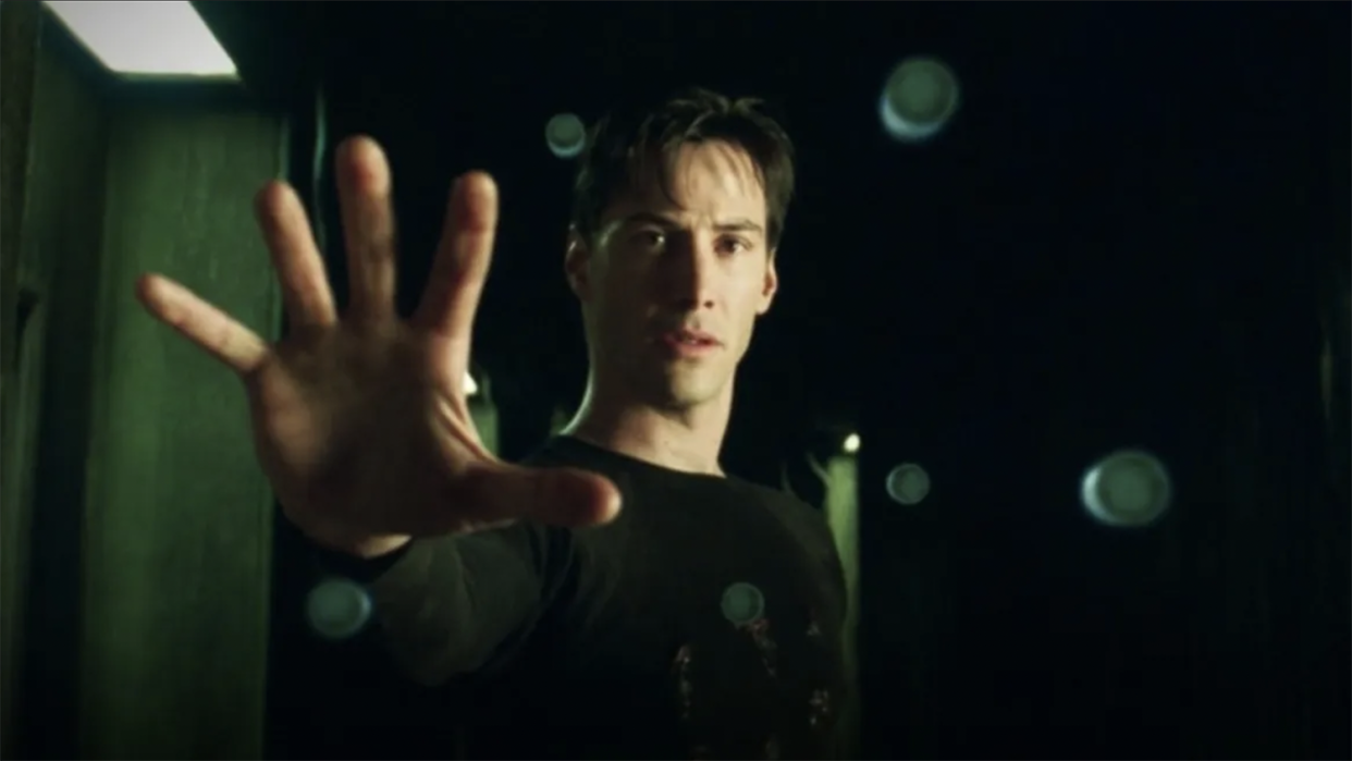  Keanu Reeves is playing Neo in The Matrix holding out his hand as objects float in the air around it. 