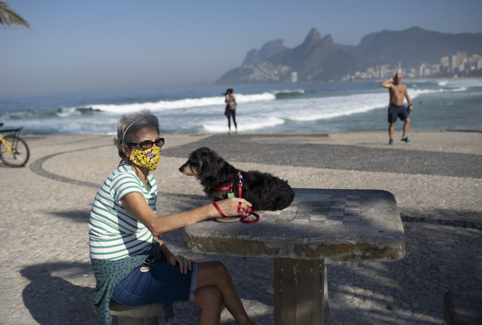 Lucia and her dog Jujuba sit at Arpoador beach, amid the new coronavirus pandemic in Rio de Janeiro, Brazil, Tuesday, June 2, 2020. Rio, the city with the second-most cases after Sao Paulo, is beginning to gradually relax restrictions on Tuesday, only allowing people to exercise on the beachfront sidewalk and practice individual activities in the sea. No one is allowed on the sand. (AP Photo/Silvia Izquierdo)
