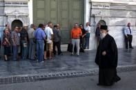 People line up outside a National Bank branch while a Greek Orthodox priest walks by in Athens, Greece, July 21, 2015. REUTERS/Yiannis Kourtoglou