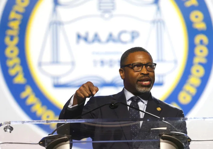 Derrick Johnson makes an emphatic point at the microphone in front of a large seal of the National Association of the Advancement for Colored People.