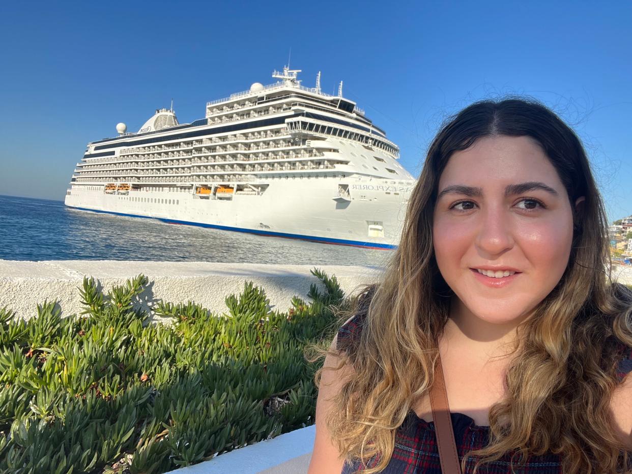 rachel dube posing for a photo with the regent seven seas explorer cruise ship in the water behind her