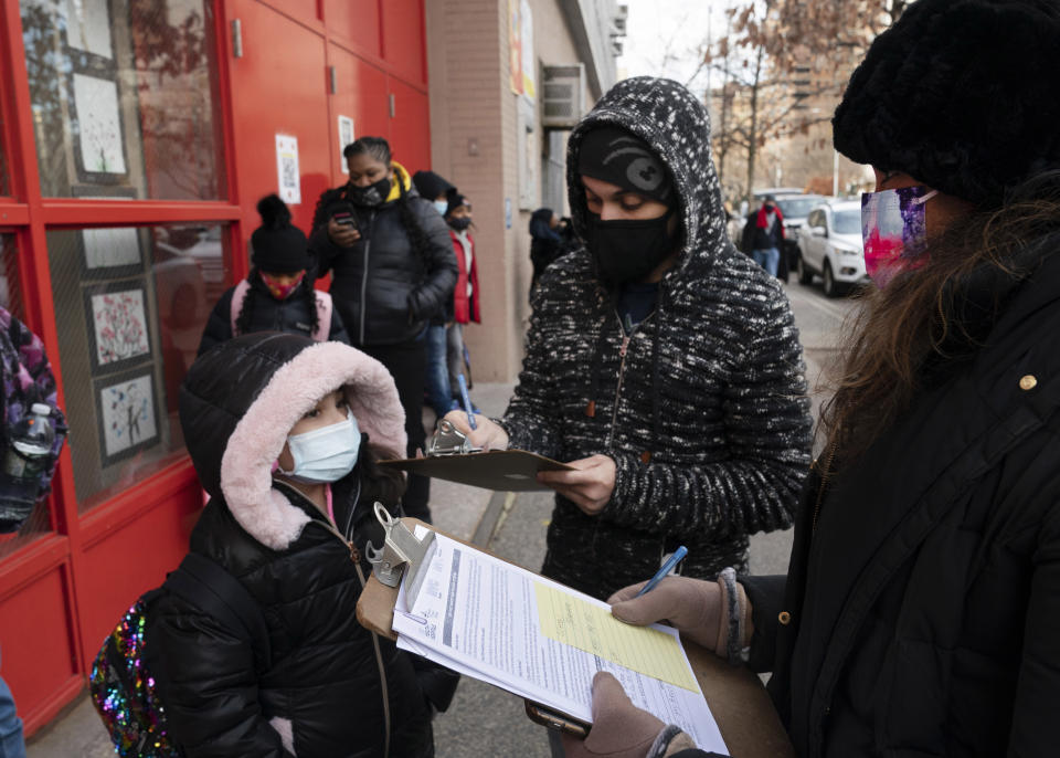 FILE - In this Dec. 7, 2020, file photo, a parent, center, completes a form granting permission for random COVID-19 testing for students as he arrives with his daughter, left, at P.S. 134 Henrietta Szold Elementary School, in New York. Children are having their noses swabbed or saliva sampled at school to test for the coronavirus in cities such as Baltimore, New York and Chicago. As more children return to school buildings this spring, widely varying approaches have emerged on how and whether to test students and staff members for the virus. (AP Photo/Mark Lennihan, File)