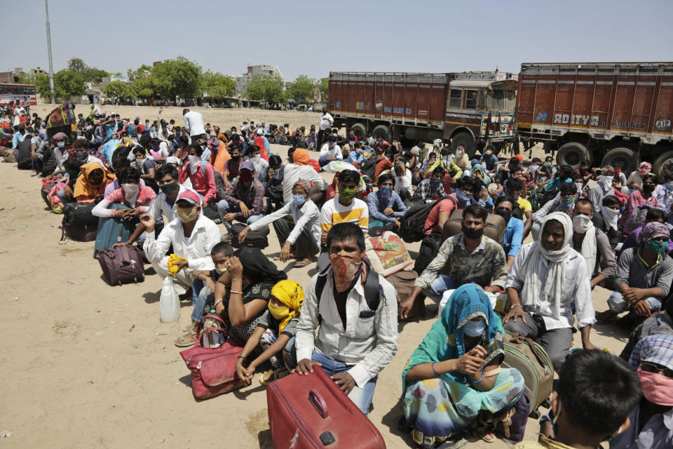 In this Wednesday, May 13, 2020, photo, migrant workers from other India states desperate to return to their homes wait for transportation to a train station in Ahmedabad, India. Tens of thousands of impoverished migrant workers are on the move across India, walking on highways and railway tracks or riding trucks, buses and crowded trains in blazing heat amid threat to their lives from the coronavirus pandemic. (AP Photo/Ajit Solanki)