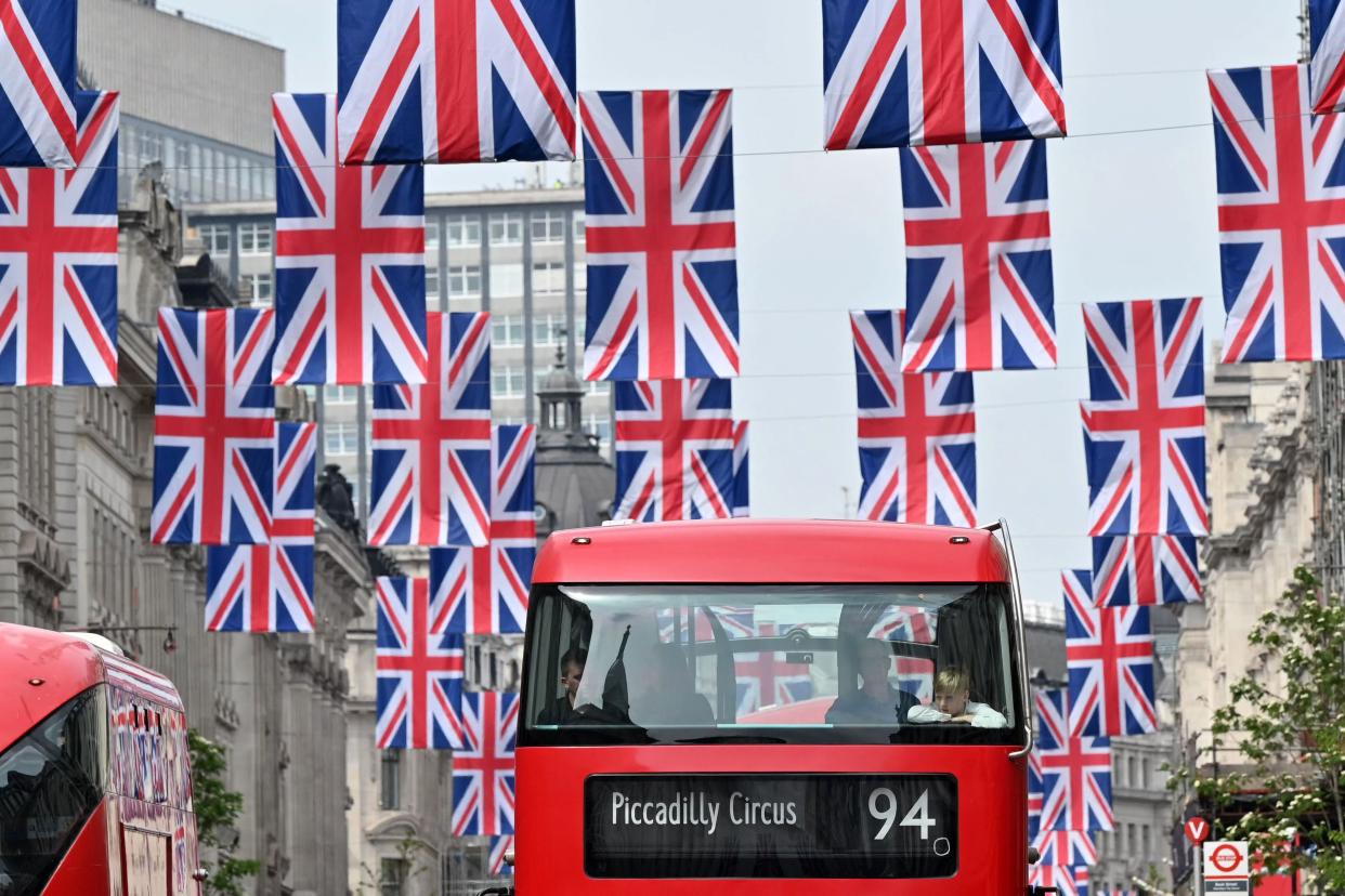 Red London buses pass beneath Union flags in central London, on April 30, 2023 ahead of the coronation ceremony of Charles III and his wife, Camilla, as King and Queen of the United Kingdom and Commonwealth Realm nations, on May 6, 2023. (Photo by JUSTIN TALLIS / AFP) (Photo by JUSTIN TALLIS/AFP via Getty Images)