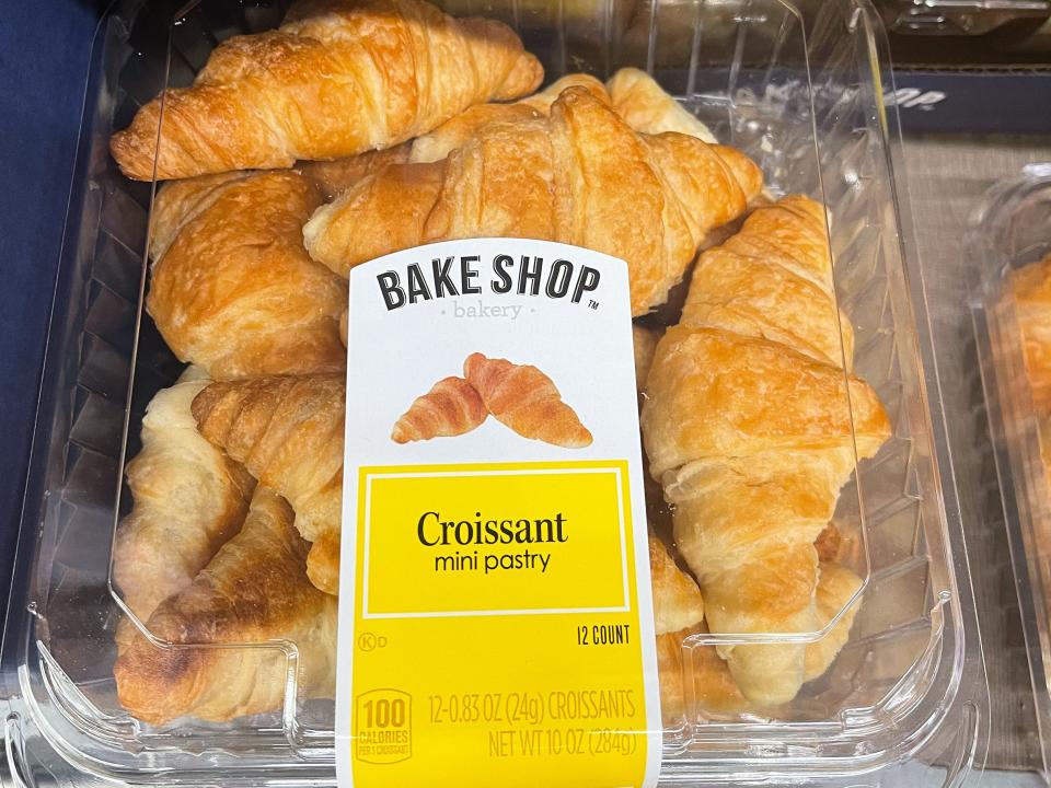 A plastic container of croissants with a white and yellow label with "Bake Shop" text