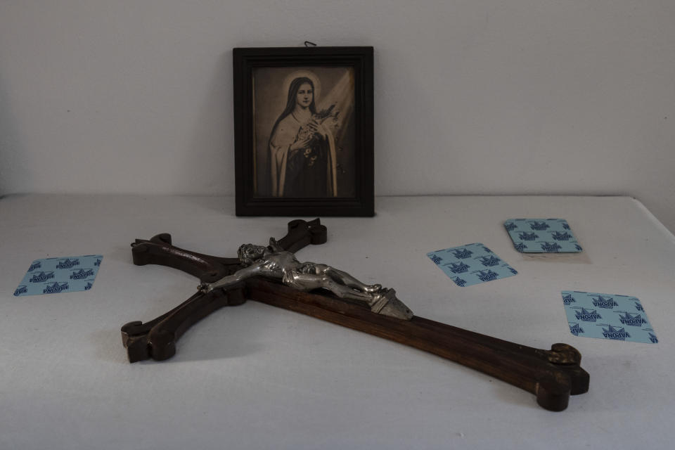 A wooden crucifix and a picture of Saint Therese of the Child Jesus and the Holy Face lie on a table inside the Dormition of the Virgin Mary Catholic Church on the Greek island of Santorini on Wednesday, June 15, 2022. The church's bell tower is a destination for tourists who flock to the island, but few are aware that a nearby monastery is home to cloistered nuns who for more than four centuries have lived in seclusion and prayer. (AP Photo/Petros Giannakouris)