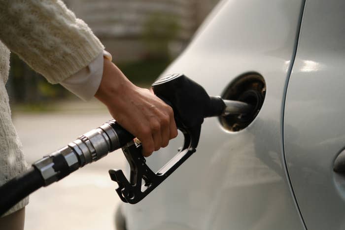 Person refuels a car at a gas pump with a hand on the nozzle