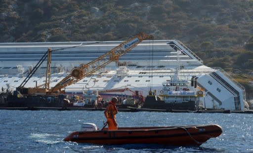 A man in a rigid inflatable boat passes by as salvage members work on a platform after removing a piece of the rock on the side of the stranded Costa Concordia cruise ship near the harbour of Giglio Porto, in July