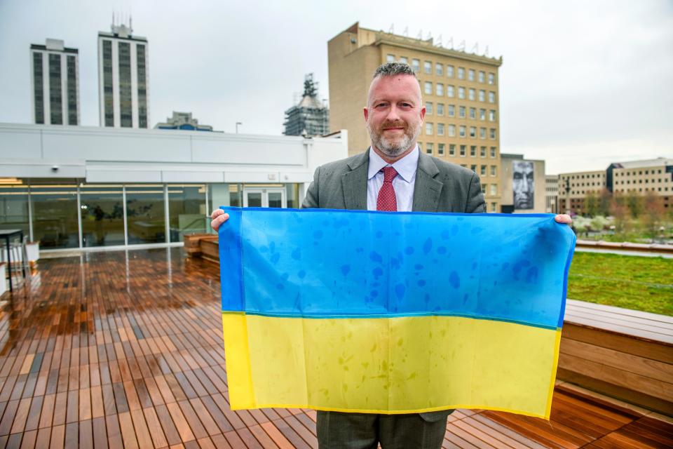 Chris Manson, vice president of government relations for OSF HealthCare, holds up a Ukrainian flag he was given during a recent trip to Ukraine. Manson organized the donation of an AMT ambulance filled with medical supplies to the besieged nation, an effort that has garnered similar donations from other parts of the United States.