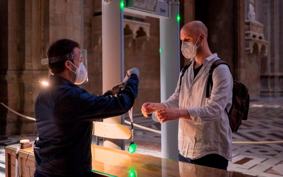 an attendant (L) handing to a visitor a new device that allows to maintain a safe distance between visitors, during testing on the eve of the museum's and Florence's Duomo reopening as the country eases its lockdown - FLORENCE MUSEUM PRESS OFFICE/AFP via Getty Images