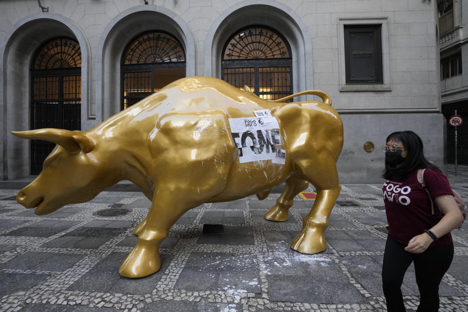 An activists walks past the Golden Bull, a replica of Wall street Charging Bull symbolizing the financial market, after her group pasted the Portuguese word "hungry" on it, outside the Brazilian B3 Stock Exchange in Sao Paulo, Brazil, Wednesday, Nov. 17, 2021. (AP Photo/Andre Penner)