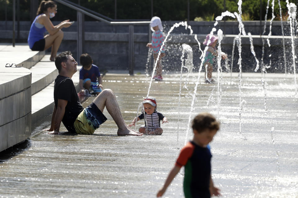 Kian Habib, of Boston, front left, relaxes in a fountain with his son, center, Tuesday, July 28, 2020, in Boston. Temperatures climbed above 90 degrees in many locations in the state Tuesday. (AP Photo/Steven Senne)
