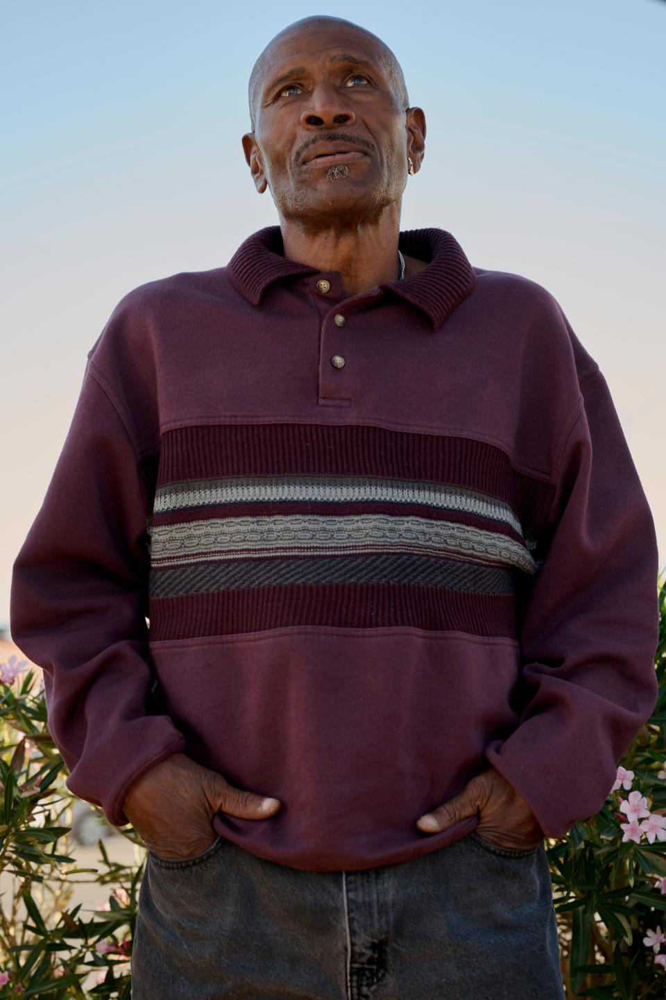 Man standing with hands in his pockets against a blue background.