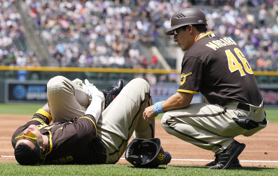 San Diego Padres first base coach David Macias, right, looks to help Manny Machado after Machado was injured while trying to run out an infield hit to Colorado Rockies starting pitcher Antonio Senzatela in the first inning of a baseball game Sunday, June 19, 2022, in Denver. Machado, who was out on the play, had to be helped from the field. (AP Photo/David Zalubowski)