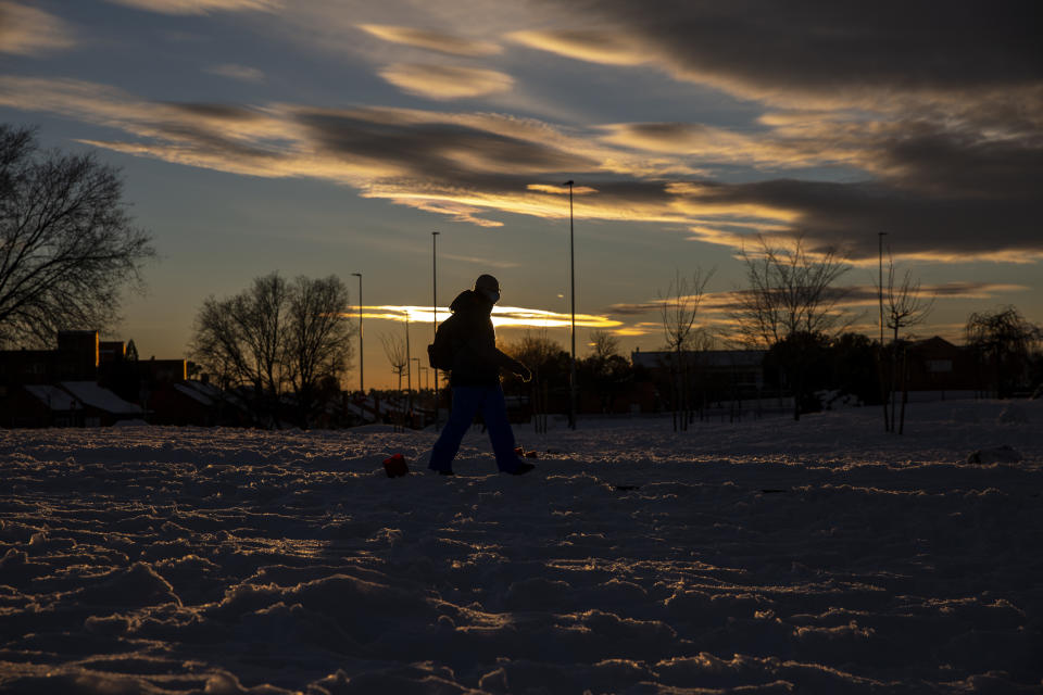 A man walks through the snow as the sunset in Rivas Vaciamadrid, Spain, Sunday, Jan. 10, 2021. A large part of central Spain including the capital of Madrid are slowly clearing snow after the country's worst snowstorm in recent memory. (AP Photo/Manu Fernandez)