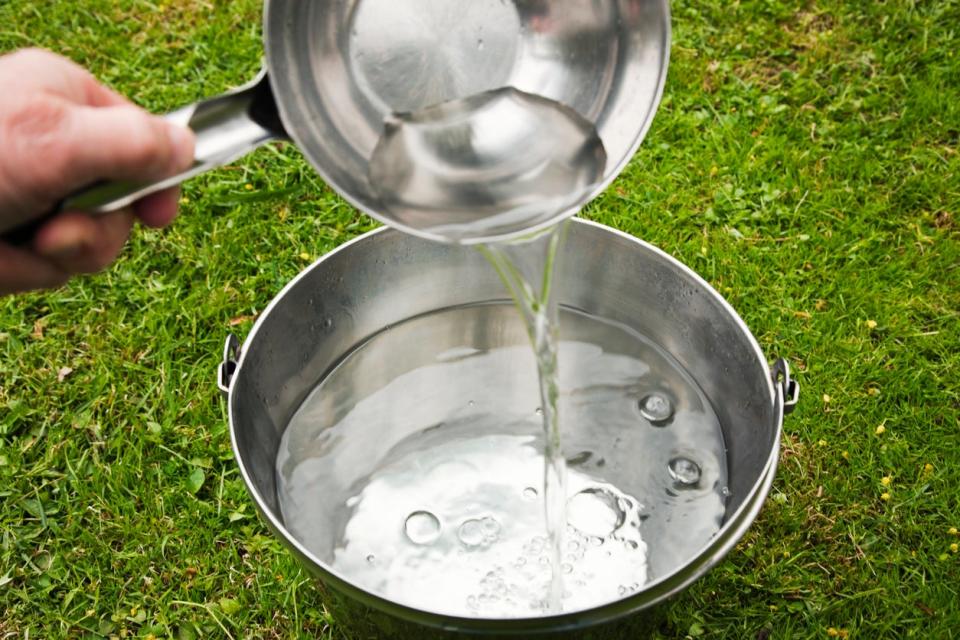 Pouring fresh clear sparkling water from ladle into a bucket placed on green lawn in the garden.