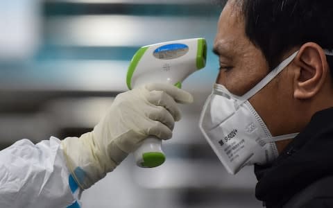 A medic takes the temperature of a man at the Wuhan Red Cross Hospital in Wuhan - Credit: AFP