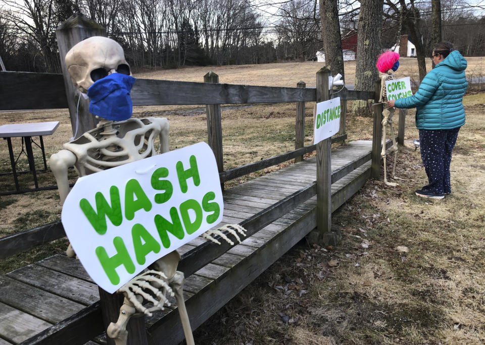 Belinda Brewer uses decorative skeletons to hold messages reminding the public of proper coronavirus preventative measures, outside her home, Wednesday, April 1, 2020, in Freeport, Maine. Gov. Janet Mills announced a statewide stay-at-home order starting Thursday in an attempt to limit the spread of coronavirus in the state.(AP Photo/Robert F. Bukaty)