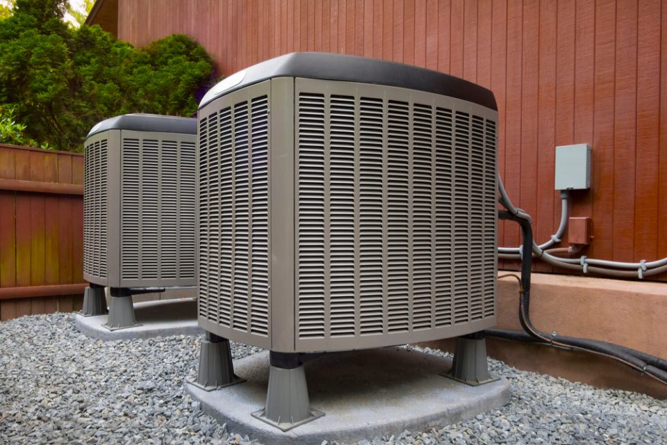 HVAC units sit in front of a red house. 