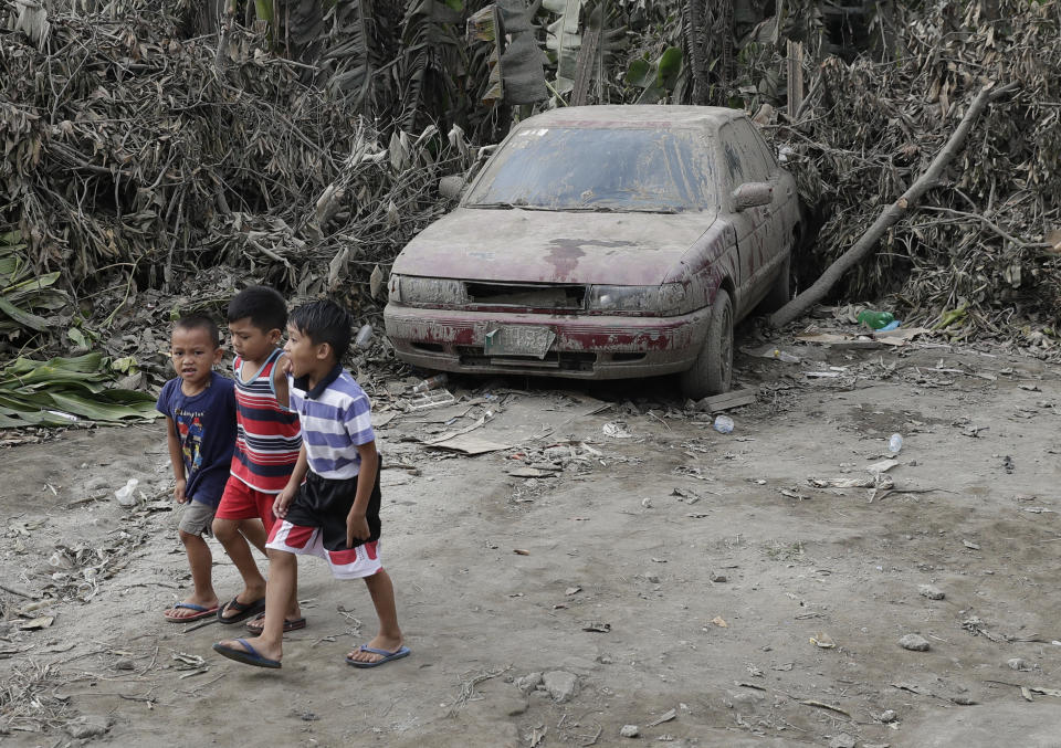 Boys pass by a car that is covered in volcanic-ash at a town near Taal volcano in Tagaytay, Cavite province, southern Philippines on Sunday Jan. 19, 2020. Philippine officials said Sunday the government will no longer allow villagers to return to a crater-studded island where an erupting Taal volcano lies, warning that living there would be "like having a gun pointed at you." (AP Photo/Aaron Favila)