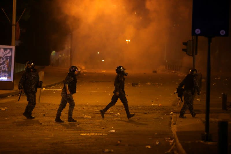 Riot police officers walk as smoke rises from tear gas, during anti government protests in Beirut