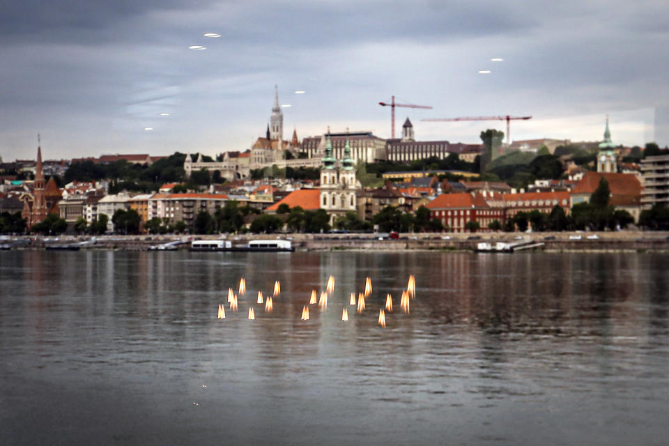 Candles are reflected in the window of a boat sailing to the Margit Bridge on the Danube river before a memorial ceremony for the victims, one year after the Mermaid boat accident, in Budapest, Hungary, Friday, May 29, 2020. Commemorations are taking place on the one year anniversary of the Danube River tragedy in which a sightseeing boat carrying mostly tourists from South Korea sank after a collision with a river cruise ship that killed at least 27 people. (AP Photo/Laszlo Balogh)