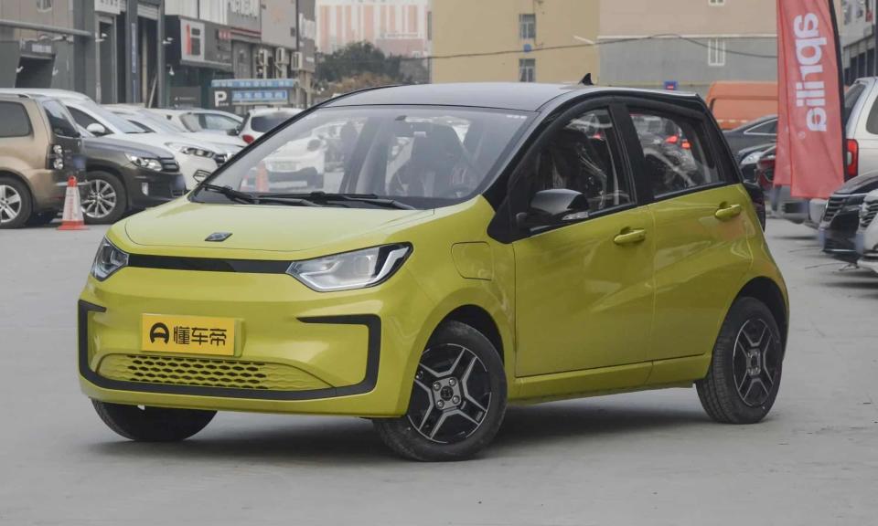The Se،l E10X, revealed earlier this year. The yellow hatchback sits in a city parking lot with parked cars and buildings behind it.