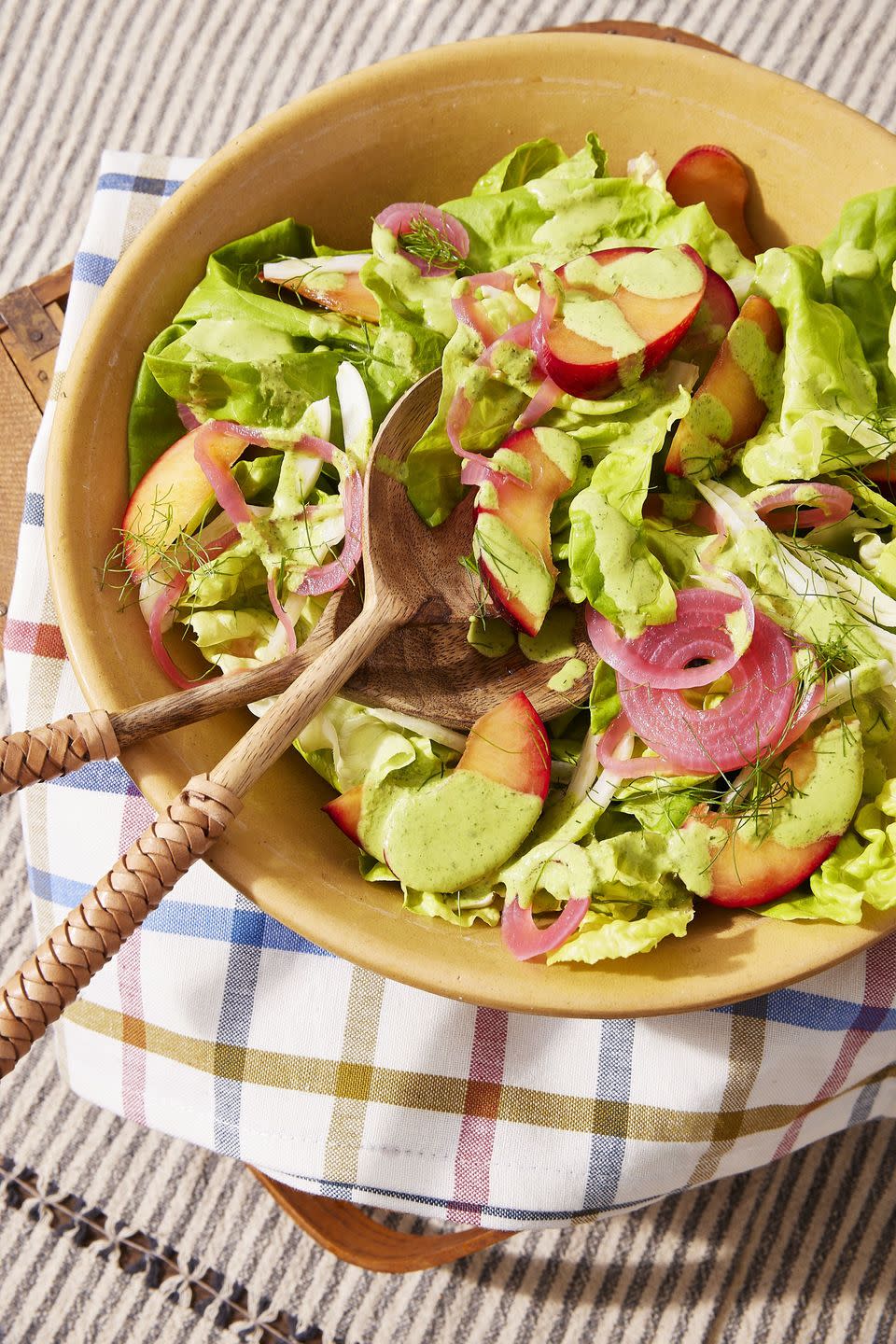 bibb salad with pickled onion, fennel, and plums in a bowl with wooden serving utensils