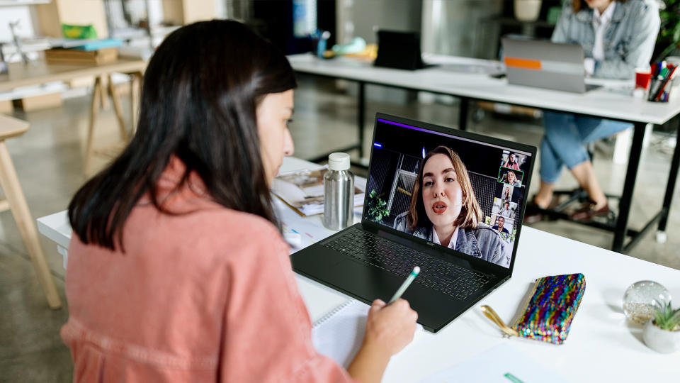 Una persona sentada en una mesa haciendo una videollamada con otra persona en un Acer Swift Edge 16. Espacio de trabajo de oficina abierto.