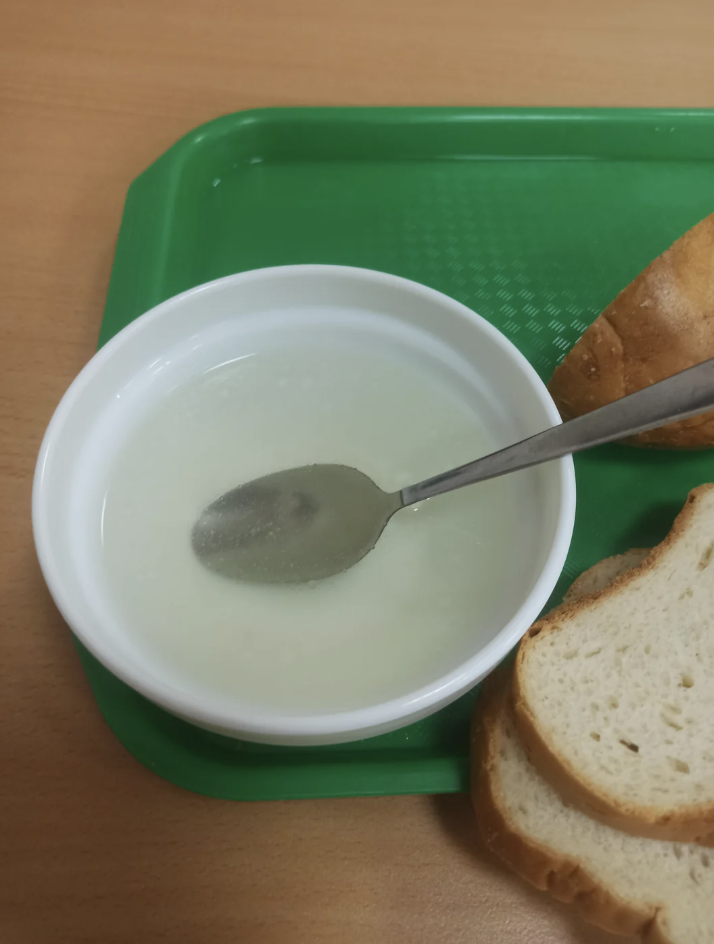 Bowl of soup with a spoon, next to sliced bread on a green tray