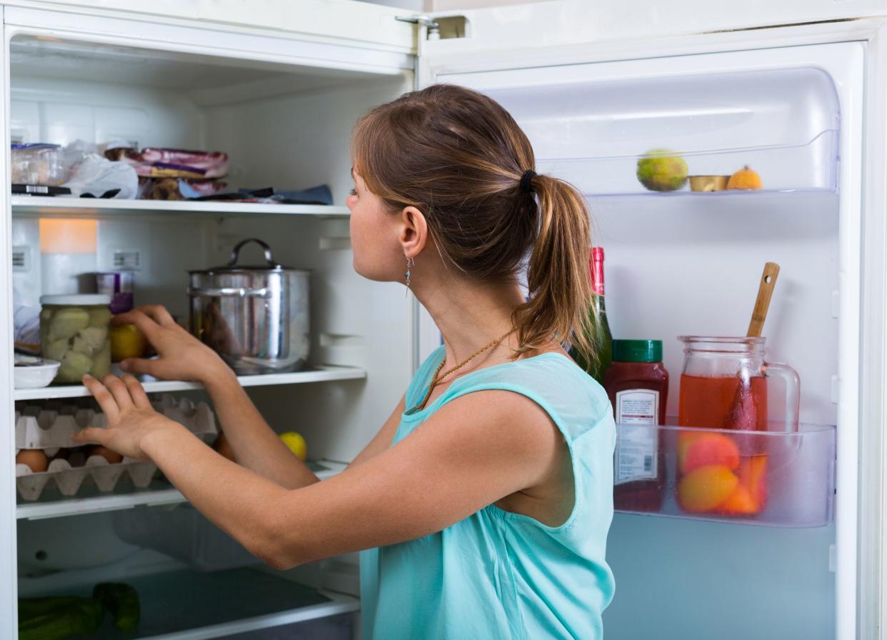 Young woman standing near refrigerator filled with products