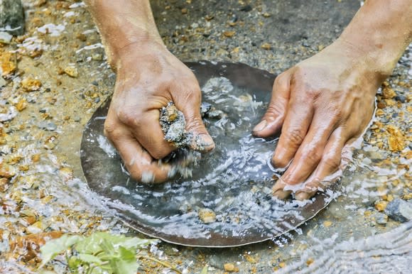 Closeup on two hands panning for gold in a rocky riverbed.